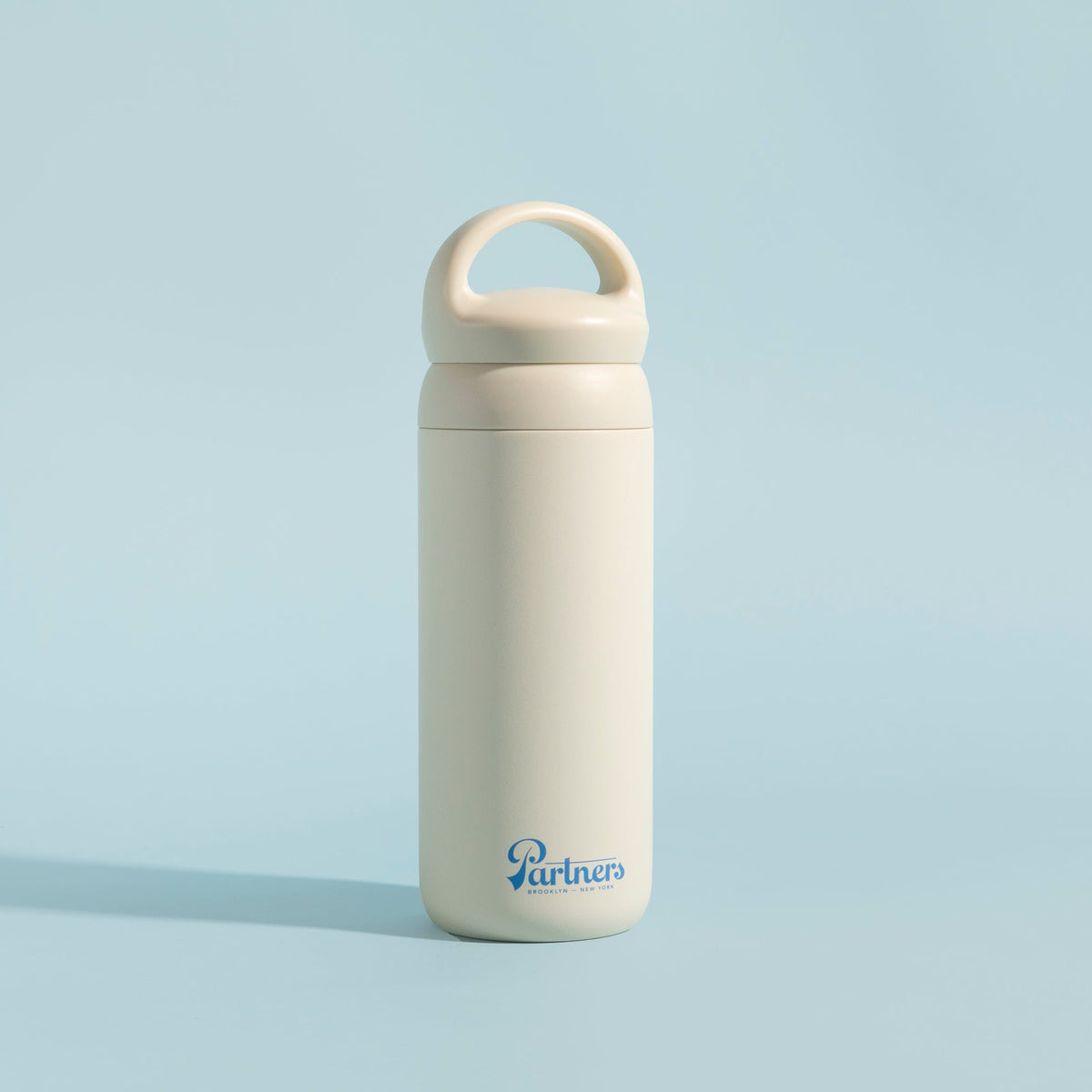 Front view of Partners x Kinto Day Off Tumbler in white showcasing its loop handle and Partners logo with a light blue background
