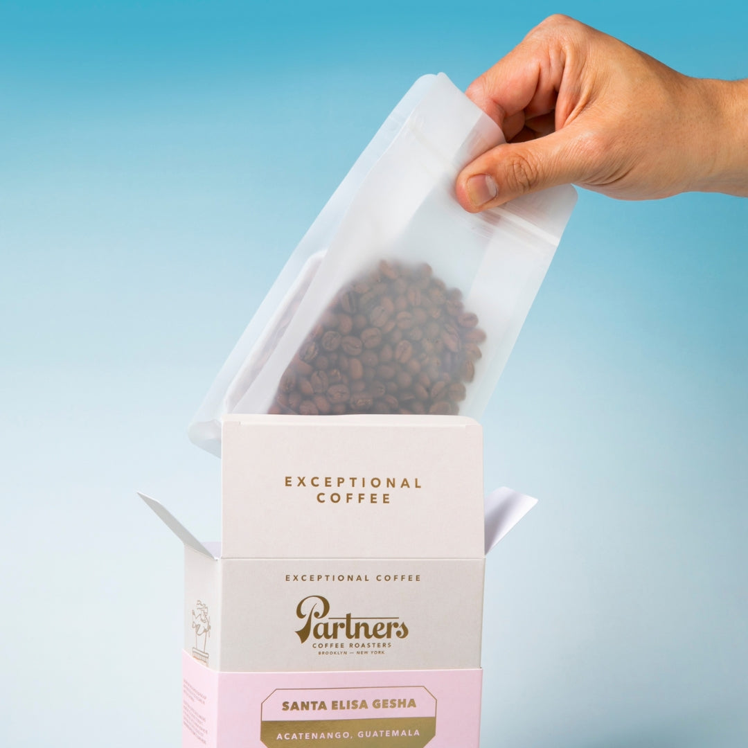 Close-up of Santa Elisa Gesha coffee package showcasing whole beans, with Partners Coffee branding against a blue background