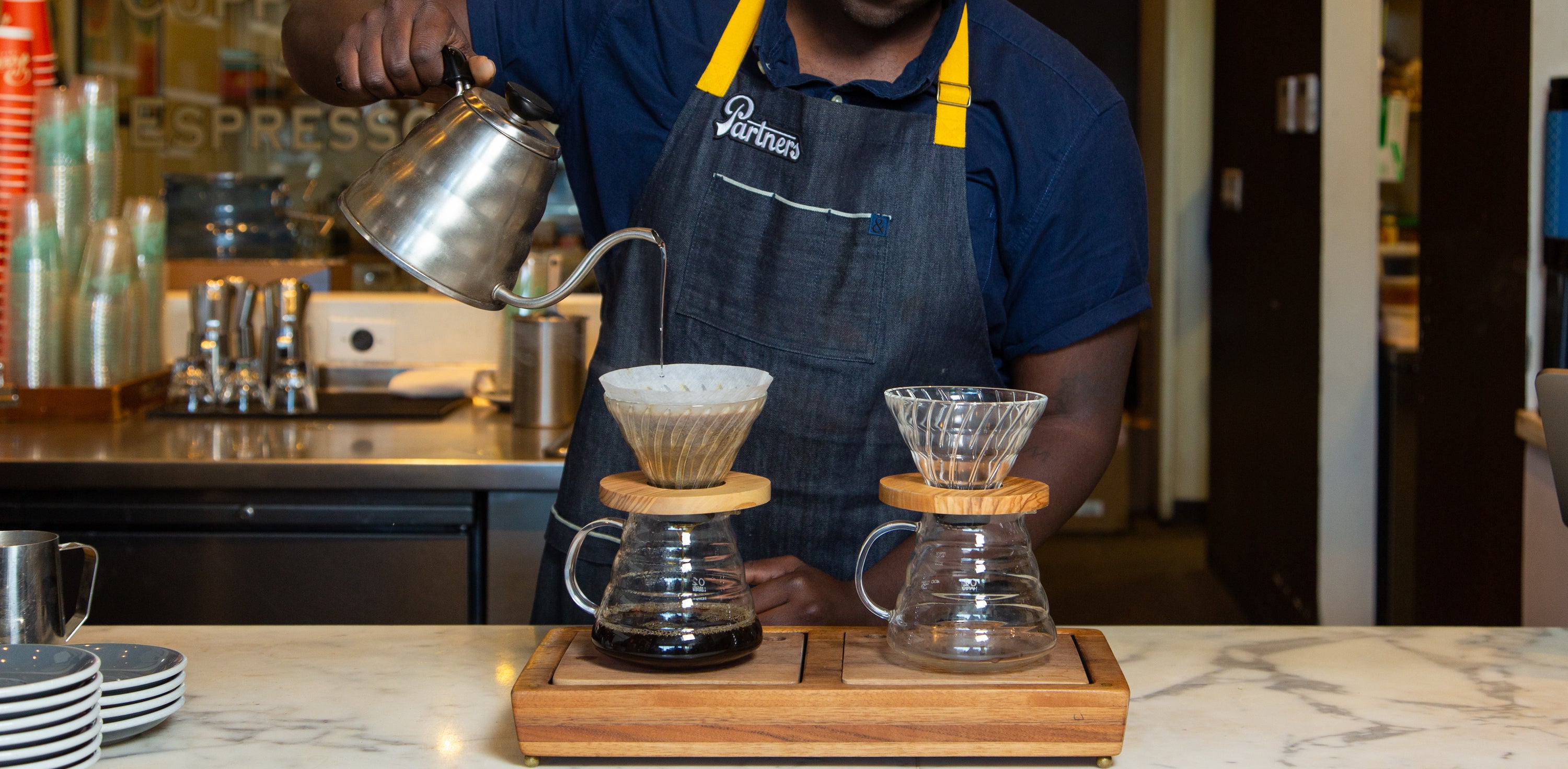 Barista pours water into two pour-over coffee brewers at a café counter